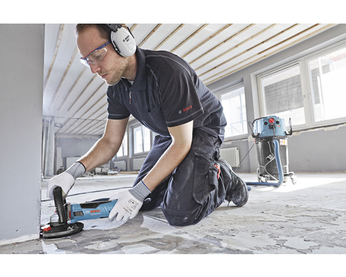 Mann mit Betonschleifer von Bosch beim Bodenschleifen in einem Raum.