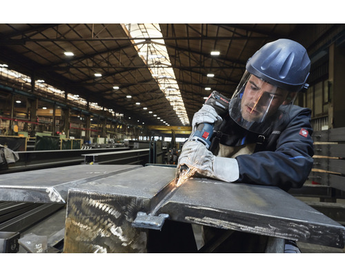 Ein Arbeiter schleift Metall mit einem Winkelschleifer in einer Fabrikhalle.