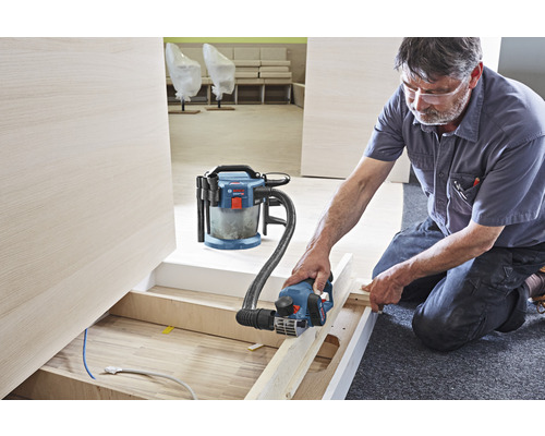 Handwerker arbeitet mit einem Elektrohobel und Staubsauger auf einer Baustelle.