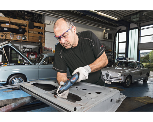 Handwerker bearbeitet Autotür mit Multifunktionswerkzeug in Werkstatt