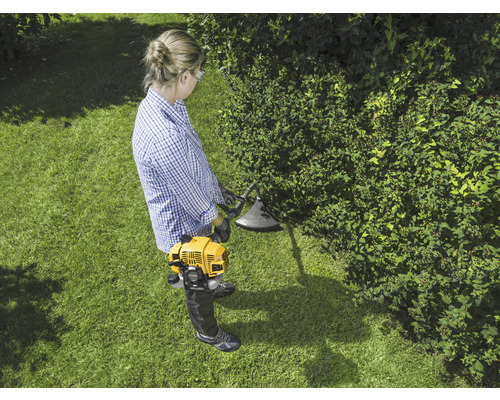 Frau arbeitet mit einem gelben Rasentrimmer im Garten.