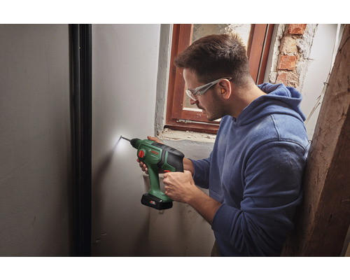 Ein Mann bohrt mit einer Akku-Bohrmaschine ein Loch in eine Wand.