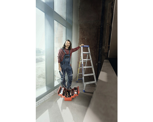 Ein Mann steht auf einer Werkzeugkiste mit Werkzeugen, neben ihm eine Leiter.