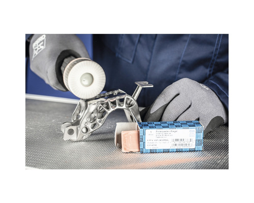 Ein Mann poliert ein Metallteil mit einer Polierscheibe, zusammen mit einem Polierpastenriegel.