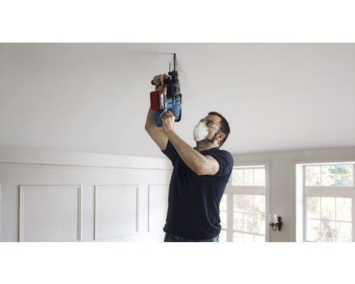 Mann bohrt mit einer Schlagbohrmaschine ein Loch in die Decke.