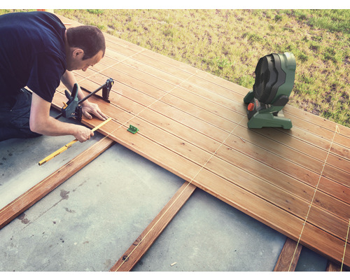 Mann verlegt eine Holzterrasse mit Werkzeugen und einem Ventilator