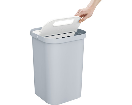 Abfallbehälter mit Deckel wird von einer Hand geöffnet.