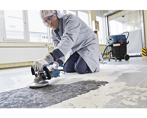Ein Mann benutzt einen Betonschleifer zur Bodensanierung in Innenräumen.