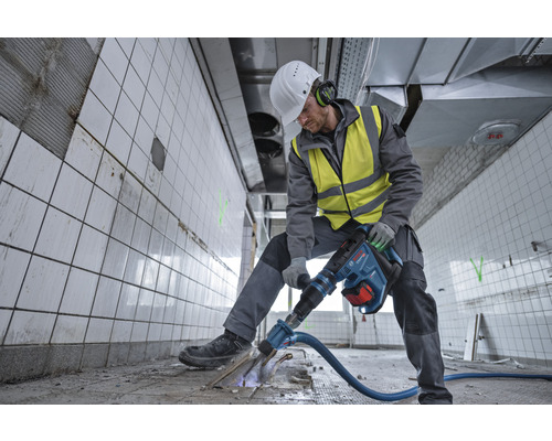 Ein Arbeiter in Schutzkleidung benutzt einen Abbruchhammer in einem gefliesten Raum.