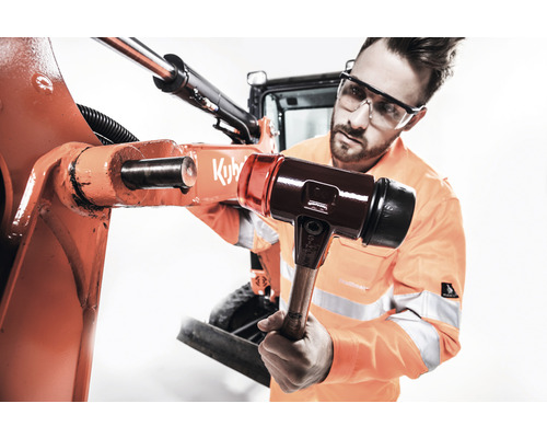 Ein Mann mit Schutzbrille verwendet einen Hammer, um eine Maschine zu reparieren.