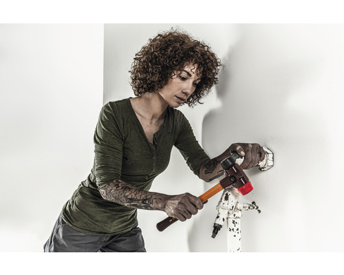 Eine Frau hämmert mit einem Hammer auf einen Dübel an einer Wand.