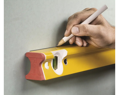 Eine gelbe Wasserwaage wird mit einem Stift an einer Wand ausgerichtet.