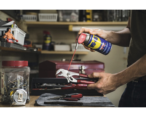 Eine Person sprüht WD-40 Multifunktionsprodukt auf eine Zange in einer Werkstatt.