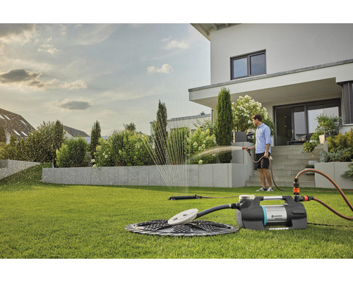 Szene mit einem Mann, der einen Garten mit einer Gartenpumpe und einem Rasensprenger bewässert