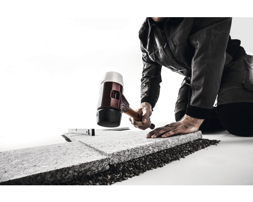Handwerker bearbeitet Steinplatten mit Gummihammer und Wasserwaage.
