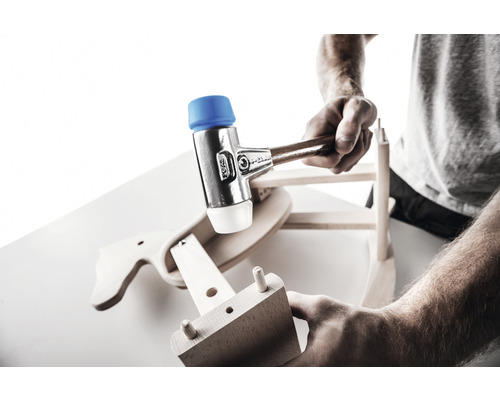 Eine Person montiert mit einem Schonhammer ein Holzspielzeug