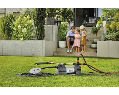 Gartenbewässerungsszene mit Gartenpumpe und Rasensprenger im Einsatz, Familie im Hintergrund