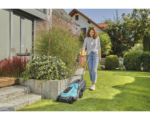 Frau bedient Rasenmäher im Garten vor dem Haus.