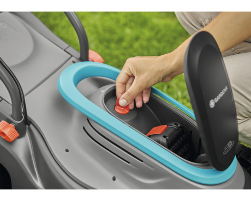 Detailansicht eines Rasenmähers mit geöffnetem Batteriefach und einer Hand, die den roten Knopf drückt.