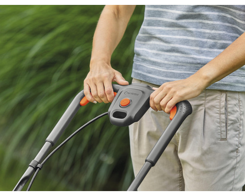 Detailaufnahme einer Person, die einen Rasenmäher mit grauen Griffen und orangefarbenen Akzenten bedient