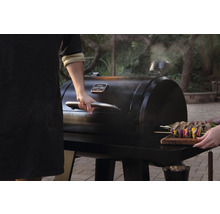 Person öffnet Holzkohlegrill mit Spießen auf einem Holzbrett