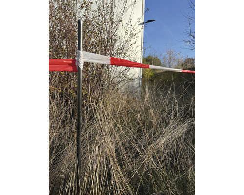 Absperrband an einem Metallpfosten vor Büschen und Gras