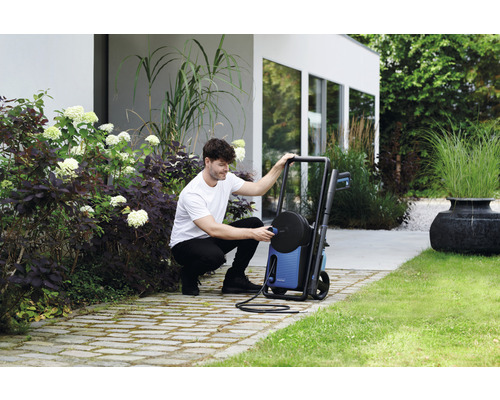 Ein Mann schließt einen Hochdruckreiniger in einem Garten an.