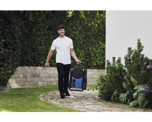 Mann trägt einen tragbaren Hochdruckreiniger im Garten.