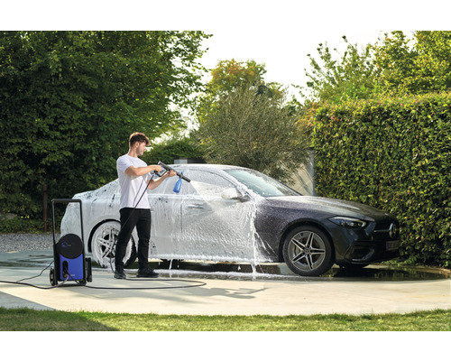 Mann reinigt Auto mit Hochdruckreiniger im Garten.