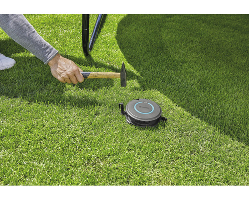 Installation eines Gardena Mähroboters mit einem Hammer auf Rasen.
