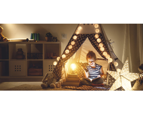 Mädchen liest in Sternenzelt mit Lichterkette und Lampe, Kuscheltier im Zimmer