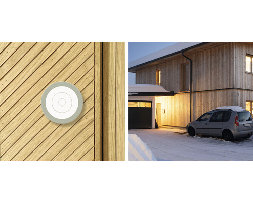 Intelligenter Lichtschalter auf Holzfassade und Ansicht eines Hauses im Winter