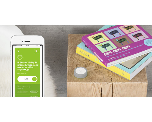 Smartphone mit App neben einem Knopf und Büchern auf einem Holzschemel