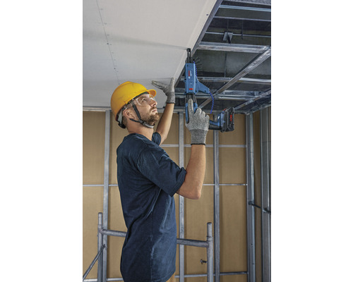 Ein Mann befestigt mit einem Trockenbauschrauber eine Gipskartonplatte an einer Decke.