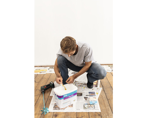 Ein Mann öffnet einen Eimer Knauf Easyputz mit einem Werkzeug.