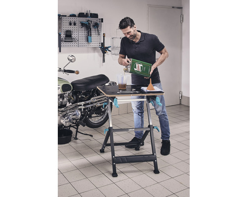 Mann füllt Öl an Werkbank in Garage um, im Hintergrund Motorrad und Werkzeugwand.