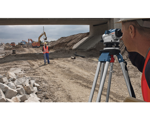 Bauarbeiter bei Vermessungsarbeiten mit einem Nivelliergerät auf einer Baustelle.