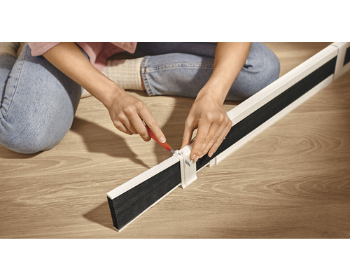Eine Person montiert eine Zugluftstoppleiste auf einem Holzboden.