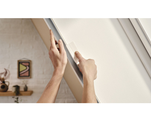 Eine Person befestigt ein Dachfenster-Verdunkelungsrollo an einem Fensterrahmen.