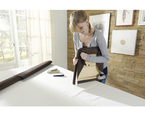 Frau polstert einen Stuhl mit braunem Möbelstoff, Tackernadeln liegen bereit.