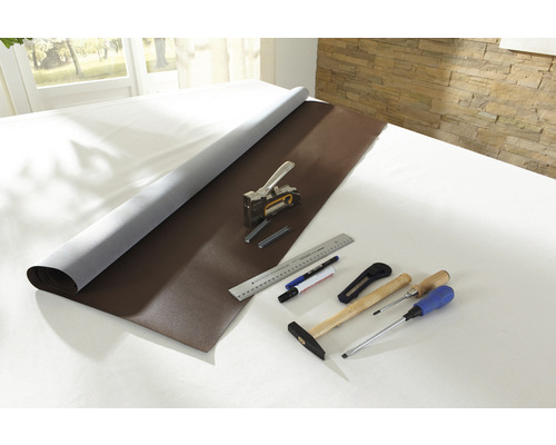 Braunes Kunstleder aufgerollt mit Werkzeugen wie Tacker, Hammer, Schraubenzieher, Messer, Lineal und Stifte auf einem Tisch