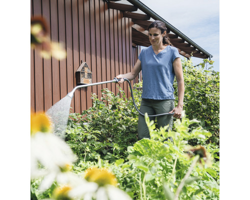 Eine Frau bewässert Pflanzen im Garten mit einem Bewässerungsstab