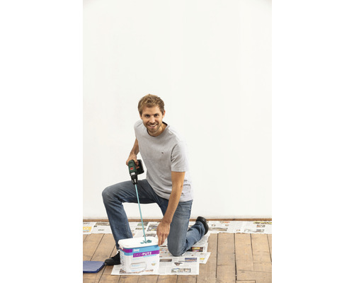 Mann kniet vor Eimer mit gebrauchsfertigem Putz und benutzt ein Rührwerkzeug zum Mischen.