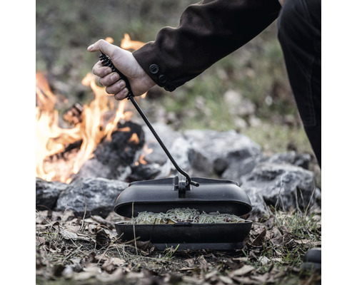 Person kocht mit einem Dutch Oven über einem Lagerfeuer