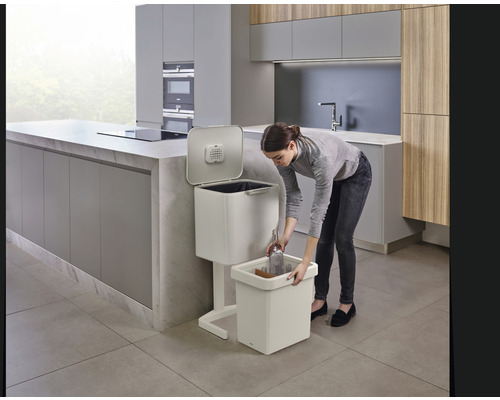 Frau wirft Glasflasche in Abfalltrennsystem in Küche.