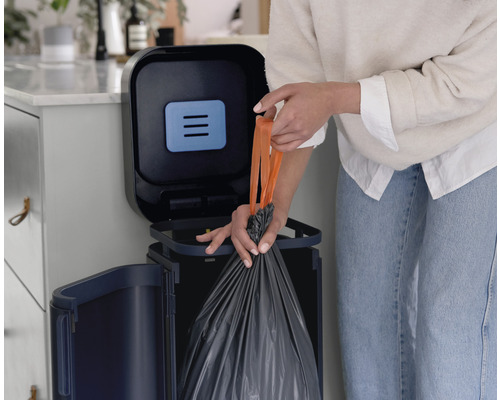 Person entsorgt Müll in einem Abfallbehälter mit Deckel.