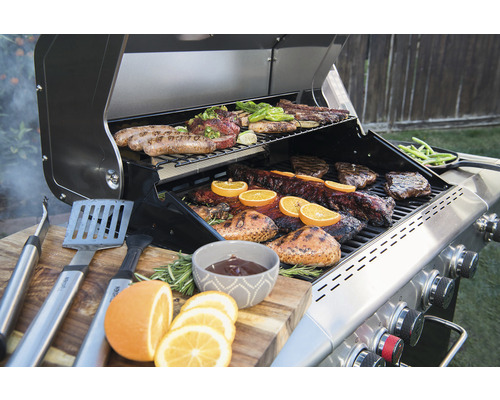 Grill mit Fleisch, Gemüse und Grillzubehör auf einem Holztisch