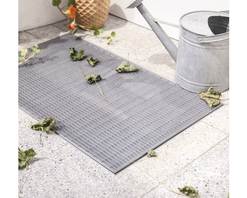 Grauer Fussabtreter aus Gitterstruktur mit Blumenvase und Gießkanne