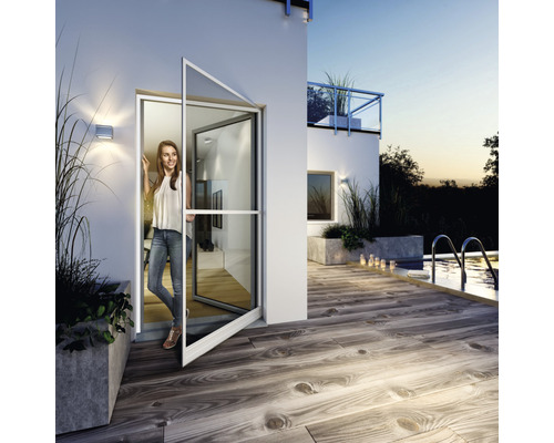 Szene mit einer Frau, die in der offenen Insektenschutztür eines Hauses steht und auf eine Terrasse mit Pool blickt.