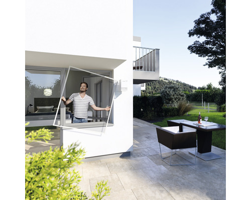 Mann befestigt Insektenschutzgitter an einem Fenster eines Hauses mit Gartenmöbeln.